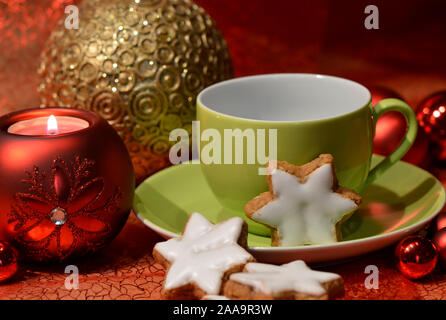 Eine grüne Schale mit sternförmigen Zimt Kekse und eine rote Christmas Ball Kerze Stockfoto