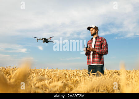 Kompakte drone schwebt vor Bauer mit Fernbedienung in der Hand. Quadcopter fliegt in der Nähe von Pilot. Agrarwissenschaftler, Luftbilder und Videos Stockfoto