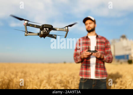 Kompakte drone schwebt vor Bauer mit Fernbedienung in der Hand. Quadcopter fliegt in der Nähe von Pilot. Agrarwissenschaftler, Luftbilder und Videos Stockfoto