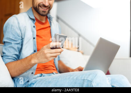 Freizeitaktivitäten zu Hause. Junge Mann sitzt auf einem Sofa plaudern auf Smartphone close-up verschwommenen Hintergrund glücklich Stockfoto