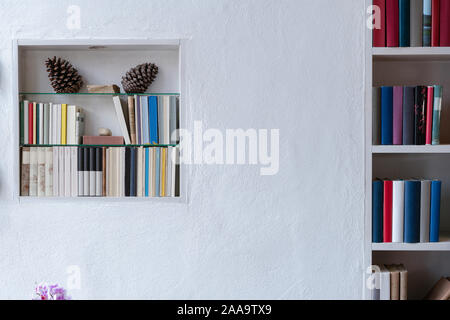 Kleines Bücherregal mit Dekoration und ein Teil der Bücherregal mit bunten Bücher in eine weiße Wand, Kopie Raum Stockfoto