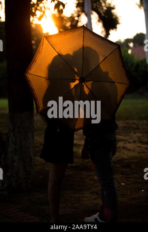 Silhouette von Paar Liebe machen bei Sonnenuntergang mit Schirm Stockfoto