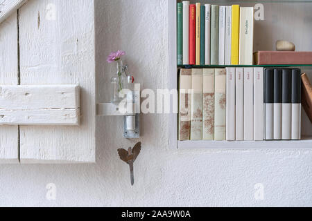 Detail aus einem Bücherregal in einer weißen Wand mit weißen Holzmöbeln Shutter, mit einer Blume in einer kleinen Glasflasche eingerichtet Stockfoto