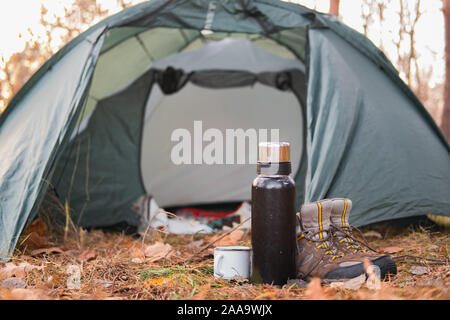 Aktive Erholung im Freien: Wandern Schuhe und warme Getränke an einem Campingplatz. Campingplatz Szene: trekking Zubehör Ständer von der Hütte in den Wald Stockfoto