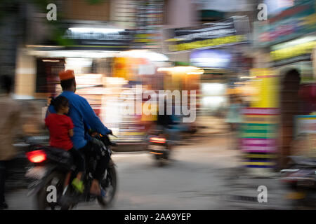 Mädchen sitzen auf dem Motorrad hinter einem Mann. Die Straßen und Geschäfte befinden sich in Bewegungsunschärfe. Stockfoto