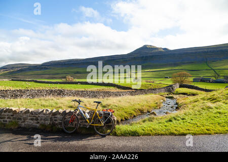 Ein Mountainbike gegen eine Mauer entlang der B 6255 mit Ingleborough Hügel im Hintergrund ruhen, Yorkshire Dales, England. Stockfoto