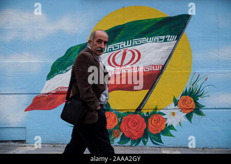 Teheran, Iran. Nov, 2019 20. Ein Iranischer Mann neben einem Wandgemälde des iranischen Nationalflagge in Teheran, Iran. Iran am 15. November die gestiegenen Kraftstoffpreise um mindestens 50 Prozent fordert Proteste in verschiedenen Städten. Präsident Hassan Rohani sagte, die Menschen des Landes besiegt hatte eine "feindliche Verschwörung'' hinter einer Welle von gewalttätigen Demonstrationen. Demonstrationen ausgebrochen in Sanktionen - schlagen Sie dem Iran in der vergangenen Woche nach einer Ankündigung der Benzinpreise um bis zu 200 Prozent angehoben werden, mit Autofahrer blockieren wichtige Straßen in Teheran vor den Unruhen rasch auf mindestens 40 städtische Ausbreitung c Stockfoto