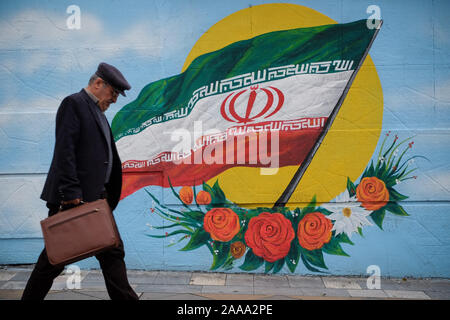 Teheran, Iran. Nov, 2019 20. Ein Iranischer Mann neben einem Wandgemälde des iranischen Nationalflagge in Teheran, Iran. Iran am 15. November die gestiegenen Kraftstoffpreise um mindestens 50 Prozent fordert Proteste in verschiedenen Städten. Präsident Hassan Rohani sagte, die Menschen des Landes besiegt hatte eine "feindliche Verschwörung'' hinter einer Welle von gewalttätigen Demonstrationen. Demonstrationen ausgebrochen in Sanktionen - schlagen Sie dem Iran in der vergangenen Woche nach einer Ankündigung der Benzinpreise um bis zu 200 Prozent angehoben werden, mit Autofahrer blockieren wichtige Straßen in Teheran vor den Unruhen rasch auf mindestens 40 städtische Ausbreitung c Stockfoto