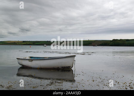 Weiß Ruderboot mit Reflexionen im Wasser mit Boote und Land unscharf im Hintergrund. Angeln Konzept Stockfoto