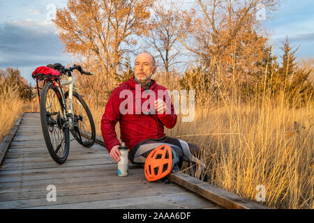 Ältere männliche Radfahrer mit einem touring Bike ist eine Erholung auf dem Holzsteg über Sumpf, Herbst Sonnenuntergang Landschaft im Norden von Colorado Stockfoto