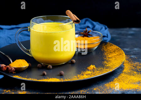 Gesunde Gelbwurz Drink mit latte Milch in einem Glas. Goldene Milch mit Gelbwurz, Ingwer, Zimt und Honig auf einem dunklen Hintergrund. Detox Stockfoto