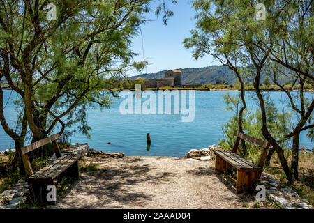 Sonniger Frühlingstag Landschaft Blick auf den Ruinen der Venezianischen Dreieck Burg in der alten Stadt im Süden Albaniens. Butrint Park - UNESCO-Welterbe. Einige Kühe, zwei Bänke unter Bäumen im Vordergrund Stockfoto