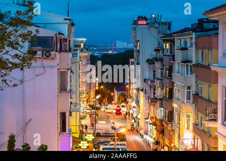 Nachtansicht von einem Fenster in der oberen Etage mit Blick auf eine geschäftige Straße in Istanbul, Türkei, mit der Bosporus-Brücke und Ortaköy Moschee beleuchtet. Stockfoto