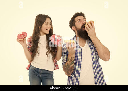 Wir haben Leidenschaft für leckere Donuts. Vater und kleine Tochter essen glasierte Krapfen. Mann und Mädchen Kind holding Ring Donuts Bärtigen. Hipster und cute kid mit gebratenen Donuts in den Händen. Stockfoto