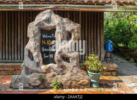 Cai, Mekong Delta, Vietnam - März 13, 2019: Entlang der Kinh 28 Kanal. Etnrance anmelden Holzskulptur von Herrn Kiet umrahmt seine historischen Haus. Blumen Stockfoto