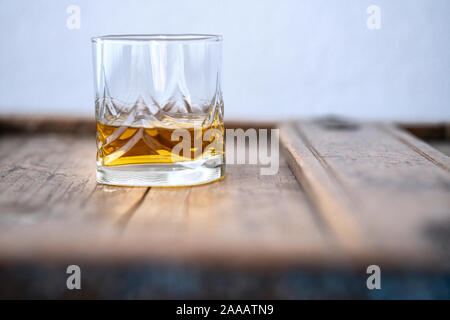 Low Angle ein Glas mit golden schimmernden Whisky auf einem alten schäbigen Holzmöbeln, Nahaufnahme, unscharfen Vordergrund Stockfoto