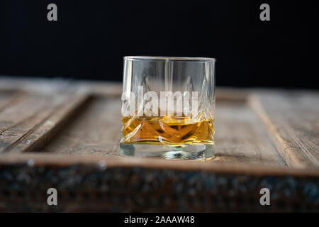 Low Angle einen Whisky Glas mit golden schimmernden Scotch auf einem alten schäbigen Holztisch Stockfoto