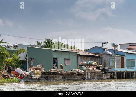 Cai, Mekong Delta, Vietnam - März 13, 2019: Entlang der Kinh 28 Kanal. Alte hölzerne Lastkahn als Junk in Beutel Lagerung schwimmende Plattform mit grünen Wellpappe Stockfoto