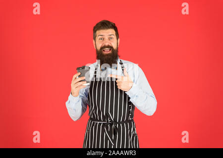 Frischer Kaffee hier. männliche Kaffee trinken. bärtiger Mann halten Sie Kaffee nehmen. brutale Kellner im Cafe. reifer Mann roten Hintergrund. Qualifizierte Diener. Barista hipster Koch Schürze. Elegante zuversichtlich Barkeeper. Stockfoto
