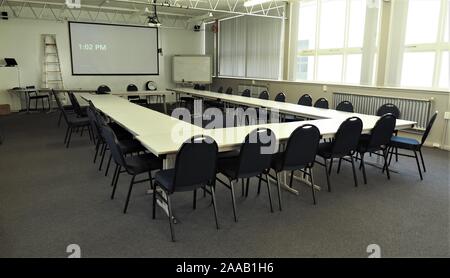 Großer und leerer Tagungsraum in typischerweise langweiliger Anordnung. Die Uhrzeit auf der Uhr (13:02 Uhr) empfiehlt die Mittagszeit und jeder geht aus. Stockfoto