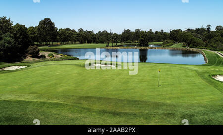 Golfplatz Fahrrinne, wassergefahr Teich, Sandbunker, Grün mit Flagge, saftig grüne Gras von Bäumen gegen den blauen Himmel umgeben Stockfoto