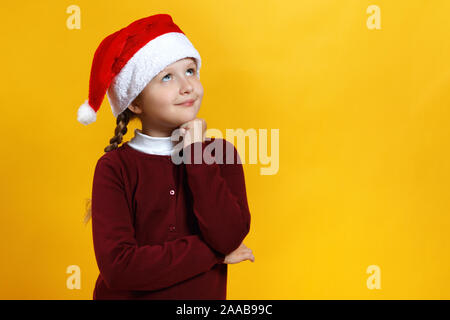 Nette charmante Baby in Santa Hut auf einem gelben Hintergrund. Kleine Mädchen träumt. Stockfoto