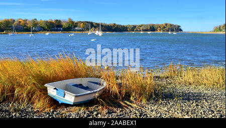 Herbsttag mit Ruderboot am Hafen Ufer mit orange braun Gras und bewaldeten entfernten Ufer im Herbst Laub. Stockfoto