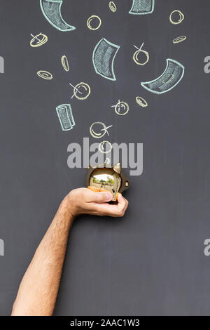 Konzept der Geld sparen mit einem goldenen Sparschwein in der Hand vor einer Tafel mit Hand gezeichnet Münzen und Banknoten gehalten Stockfoto