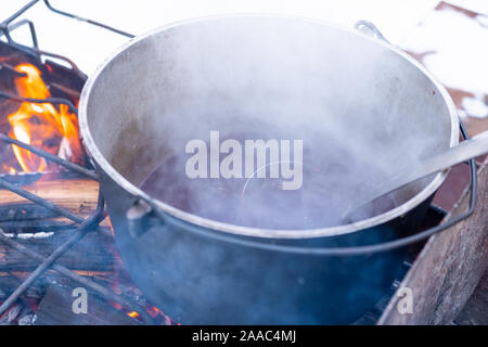 Bei einem Feuer in einem Topf Vorbereitung Glühwein. Hot rot Wein am offenen Feuer im Winter Stockfoto