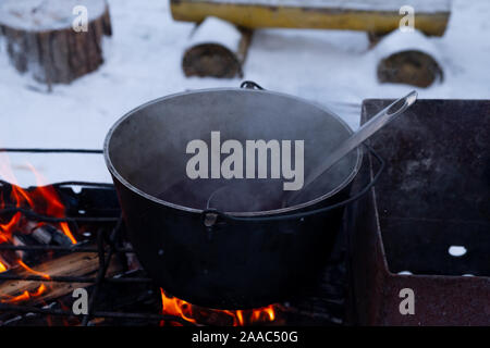 Bei einem Feuer in einem Topf Vorbereitung Glühwein. Hot rot Wein am offenen Feuer im Winter Stockfoto