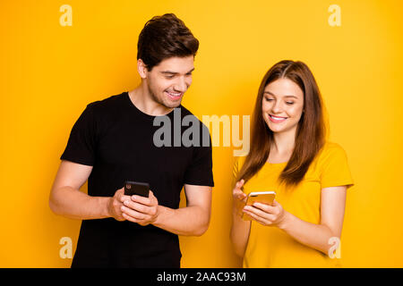 Foto fröhliche, positive niedlich charmant Schön influencers sharing Erfahrung zwischen einander in Schwarz Gelb t-shirt Holding Telefone suchen Stockfoto