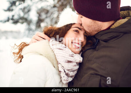Der Kerl küsst ein lächelndes Mädchen im Winter im Schnee Stockfoto