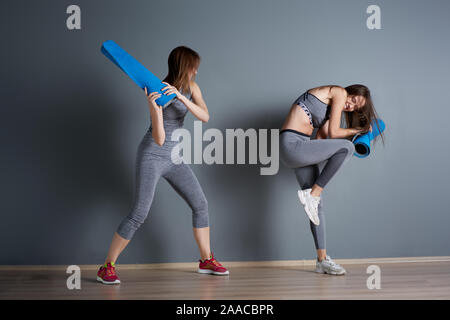 Sportliche Frauen kämpfen Twisted blaue Teppiche gegen graue leere Wand in der Turnhalle Stockfoto