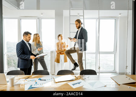 Eine Gruppe von jungen, kreativen Mitarbeitern in einige informelle Diskussion, während in der hellen Tagungsraum mit grossen Fenstern Stockfoto