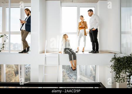 Eine Gruppe von jungen, kreativen Mitarbeitern in einige informelle Diskussion, während in der zweistufige helle Tagungsraum mit grossen Fenstern Stockfoto