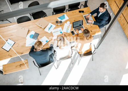 Geschäft Leute arbeiten mit Computern und einige gedruckte Statistiken auf dem hölzernen Tisch im Konferenzraum, Ansicht von oben Stockfoto