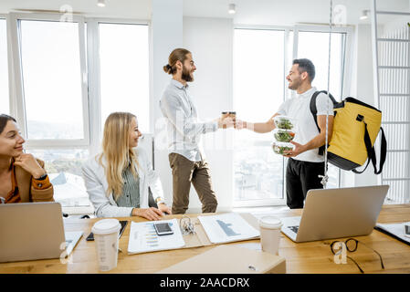 Kurier liefern gesunde Geschäftsessen mit thermal Bag für die Mitarbeiter, indem Sie ihnen Snacks zum Mitnehmen in den weißen Büro Stockfoto