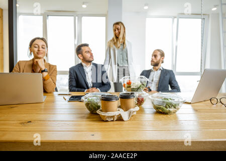 Mitarbeiter im Büro sitzen im Büro mit Geschäftsessen im Vordergrund. Konzept der gesunden Essen zum Mitnehmen auf der Arbeit Stockfoto