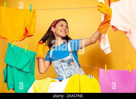Lustige und schöne Hausfrau Hausarbeit tun auf gelbem Hintergrund. Junge kaukasier Frau durch gewaschene Kleidung umgeben. Das häusliche Leben, helle Artwork, allgemeine Ordnung und Sauberkeit. Die selfie. Stockfoto