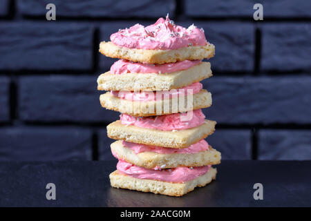Stapel von süßen Shortbread Cookies gekrönt mit Strawberry vanilla buttercream Frosting bestreut mit essbaren Silber Perlen und geschreddert Coconut Stockfoto