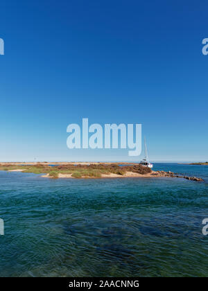 Ein Katamaran günstig in einer der kleinen Buchten zwischen den verschiedenen Inseln Ilha da Culatra an der Algarve in Portugal. Stockfoto