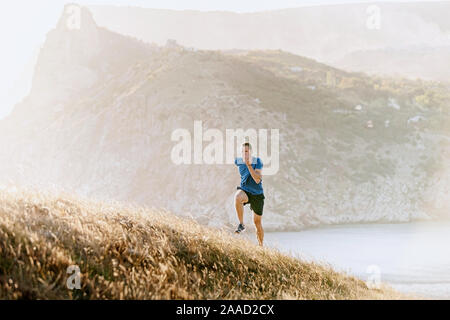 Männliche Läufer laufen bergauf im Sonnenuntergang Meer Bay Stockfoto