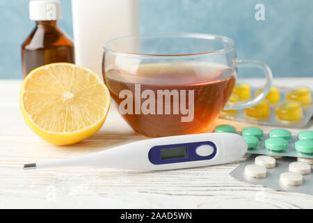 Verschiedene Tabletten, Thermometer, medizinische Flaschen, Tee und Zitrone auf weißem Hintergrund Holz, Nahaufnahme Stockfoto