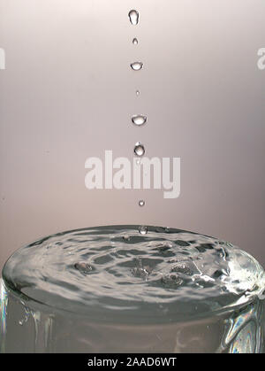 Tropfen im Glas voll Wasser fallen Stockfoto