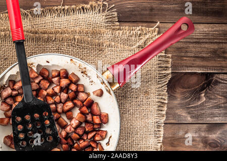 Gebratene Würstchen in Scheiben in einem Würfel auf einer Pfanne auf einem hölzernen Hintergrund. Stockfoto