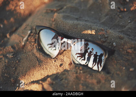 Die Sonnenbrille an einem Sandstrand im Sommer, und der blaue Himmel mit Menschen ist in Gläsern wider. Stockfoto