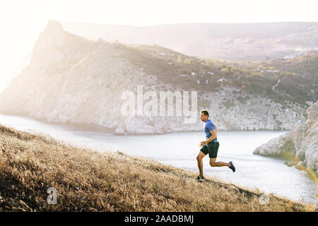 Athleten laufen bergauf im Sonnenuntergang am Meer Bucht im Hintergrund Stockfoto