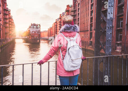 Ansicht der Rückseite des erwachsenen Frau Tourist mit Rucksack Sonnenuntergang auf der Brücke in der historischen Speicherstadt Speicherstadt. Hamburg, Deutschland, Europa. Stockfoto