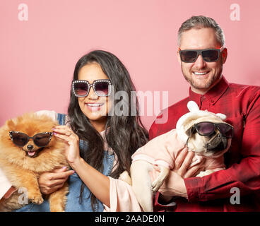 Das Lächeln des Mannes und der Frau in der Sonnenbrille mit spitz und Mops in seine Hände auf leere rosa Hintergrund im Studio Stockfoto
