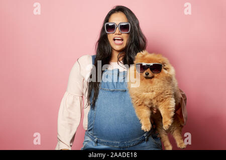 Junge Brünette in Sonnenbrille mit Ingwer spitz auf leere rosa Hintergrund im Studio Stockfoto